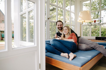 Happy couple relaxing on couch, using smartphone