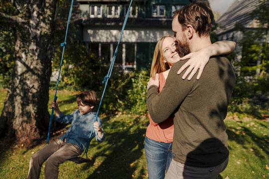 Son swinging in garden with parents kissing next to him