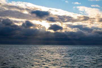 blue dark stormy clouds above the sea, the sun rays breaks through the clouds