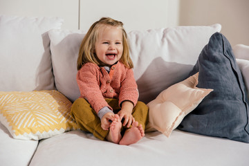 Laughing little girl sitting on couch at home