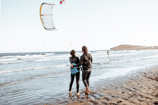 Couple of kitesurfers catching airflow with kite on the beach, view from the backside