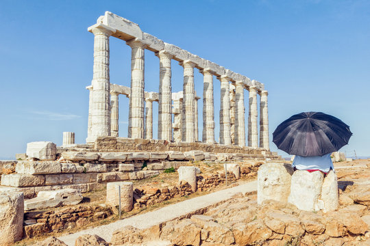 Tourist looking at ancient ruin of Poseidon temple, Cape Sounion, Attika, Greece