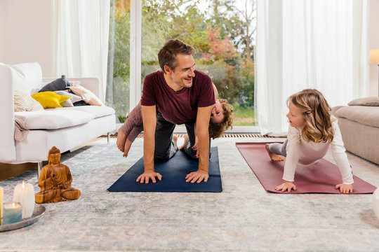 Father with daughters doing yoga in living room at home