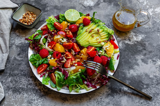 Studio shot of fruity salad plate with lambs lettuce, radicchio, lettuce hearts, avocado, tomato, pine nuts, raspberries, oranges, lime