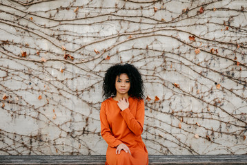 Portrait of a beautiful young woman wearing a dress in front of concrete wall with climbing plant