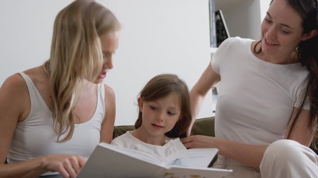 Same Sex Female Couple Reading Book With Daughter At Home Together