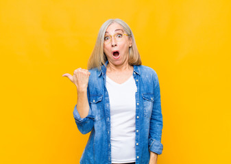 senior or middle age pretty woman looking astonished in disbelief, pointing at object on the side...