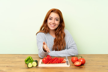 Teenager redhead girl with vegetables in a table handshaking after good deal