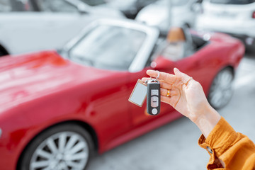 Woman holding keychain of a new purchased or leased red car at the parking place outdoors, close-up...