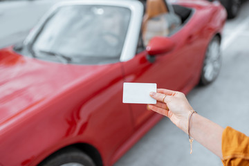 Woman holding plastic card with empty space to copy paste with red car on the background. Vehicle...