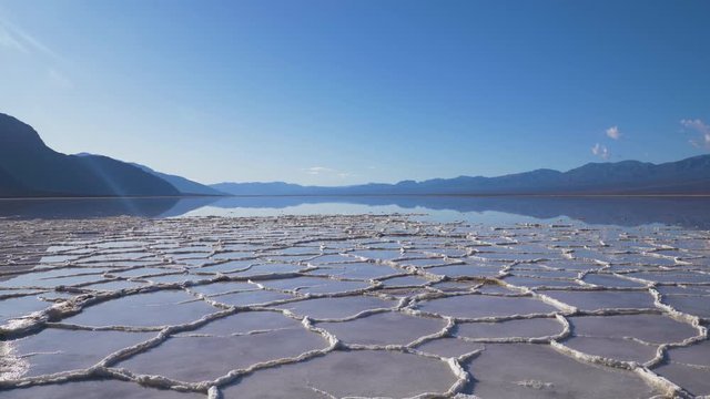 Badwater Basin at Sunny Day. Salt Crust Formations with Water and Blue Sky. Death Valley National Park. California, USA. Panning