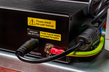 Installed on mounting plate electrical appliance in black metal case connected by black wire to the power supply and grounded by yellow and green wire. Close-up view