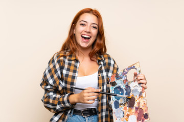 Teenager redhead girl holding a palette over isolated background