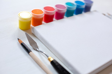 Art canvas with cans of acrylic paint and art brushes.  White canvas