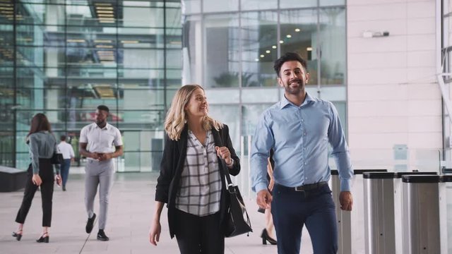 Businessman And Businesswoman Walking Through Lobby Of Busy Modern Office