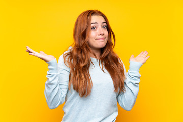 Teenager redhead girl over isolated yellow background making doubts gesture