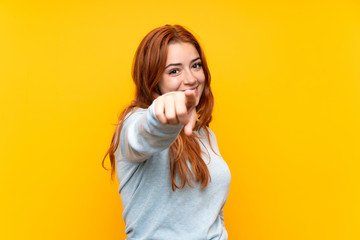 Teenager redhead girl over isolated yellow background points finger at you with a confident...