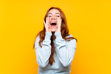 Teenager redhead girl over isolated yellow background shouting and announcing something