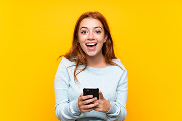 Teenager redhead girl over isolated yellow background surprised and sending a message