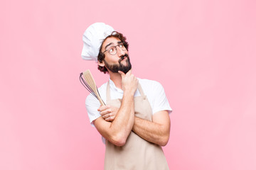 young crazy baker man with a cook tool against pink wall