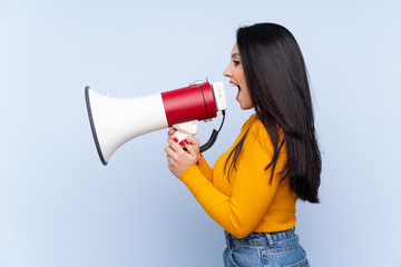 Young Colombian girl over isolated blue background shouting through a megaphone