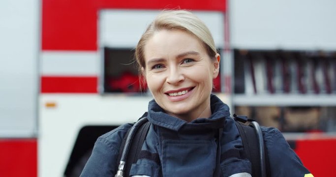 Close up of the Caucasian pretty blond woman firefighter turning face to the camera and smiling cheerfully. Portrait.