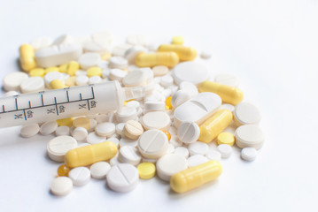 A bunch of yellow and white tablets, pills isolated on a white background with syringe. close up. Selective focus. Health day. Copyspace