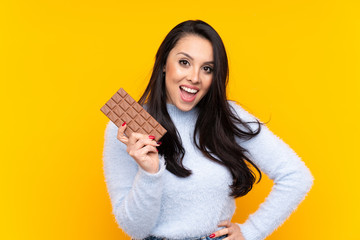 Young Colombian girl over isolated yellow background taking a chocolate tablet and happy