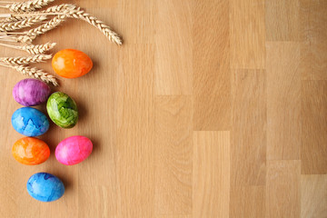 Naklejka na ściany i meble colored painted eggs and wheat ears lie on a wooden table, easter concept