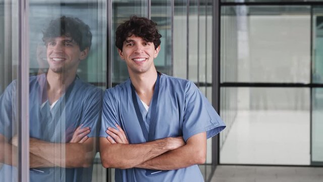 Portrait Of Male Doctor Wearing Scrubs Standing In Modern Hospital Building