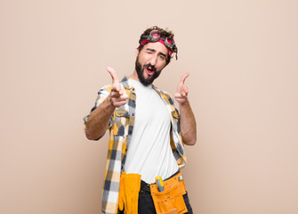 young housekeeper man feeling happy, cool, satisfied, relaxed and successful, pointing at camera,...