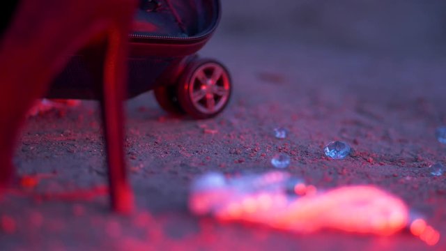 Shallow rack focus on high heels, diamonds & broken pearls on red light ground grunge scene.