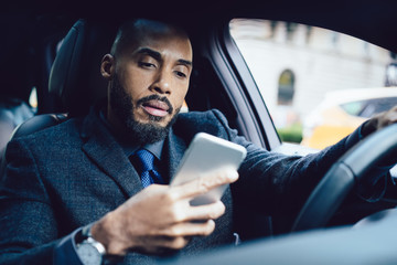 Puzzled adult ethnic executive man using smartphone in car