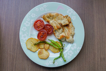 Grilled chicken meats, tomatoes, peppers and potatoes on a plate on the wooden table. 