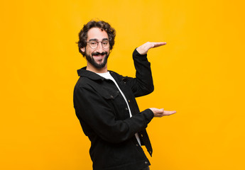 young crazy handsome man smiling, feeling happy, positive and satisfied, holding or showing object or concept on copy space against orange wall © kues1