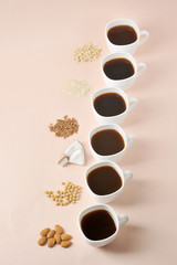 Cups of black coffee and ingredients for alternative milk: coconut, soybeans, almond, rice, buckwheat, oatmeal.  Concept lactose-free vegetable milk for cappuccino.  Light background. Vertical frame.