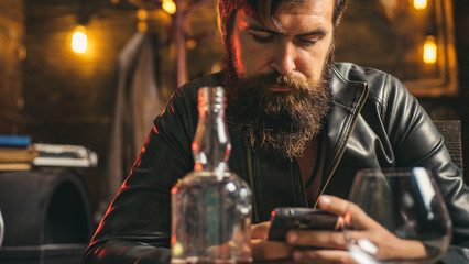 Lifestyle of modern businessman. Handsome bearded businessman is drinking expensive whiskey. Macho man scrolling news feed in his smartphone.