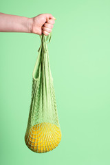 Yellow melon hanging in reusable mesh shopping bag. Buying fruit