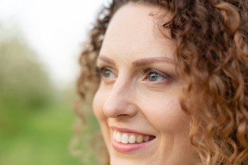Fototapeta premium Close up portrait of young smiling attractive woman with curly hair in green flowering spring park. Pure emotions.