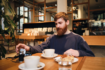 Fototapeta na wymiar Young handsome bearded man having coffee break in cafe