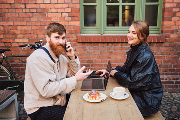 Young couple joyfully working together during coffee break in street cafe