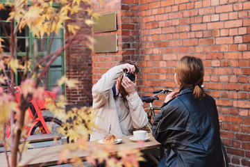 Young man taking photo of girlfriend during coffee break in cafe outdoor