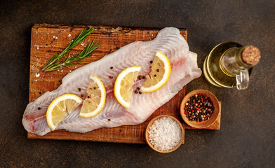  raw pangasius fillet on a cutting board with lemon, oil and spices on a stone background. raw fish.
