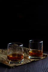 alcoholic drinks. glass of whiskey with ice on a black background. two glasses of whiskey on a wooden table with burlap.