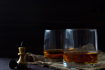 alcoholic drinks. glass of whiskey with ice with chess pieces on a black background. two glasses of whiskey on a wooden table with a burlap chess queen and a pawn. horizontal orientation