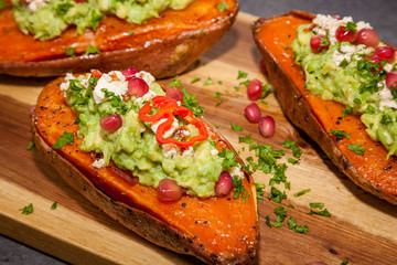 Healthy food - Baked sweet potatoes served with guacamole, feta cheese and pomegranate