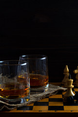alcoholic drinks. glass of whiskey with a chess queen and pawn on a black background. two glasses of whiskey on a chessboard with chess pieces. vertical orientation