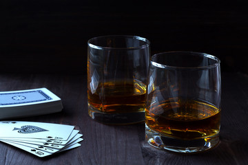 alcoholic drinks. glass of whiskey on a black background. two glasses of whiskey on a wooden background with a deck of cards. horizontal orientation