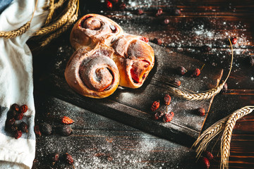 Sweet pastry removed from the oven with strawberry jam and pressed with sugar powder on an old wooden background with wheat ears and  hip rose .