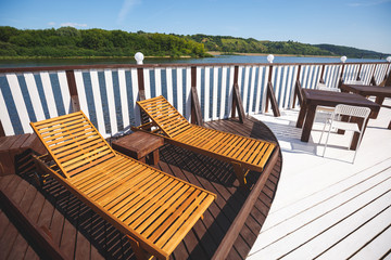 Wooden deck chairs on the landing stage. A place of rest in the open air. Stylish wooden tables....